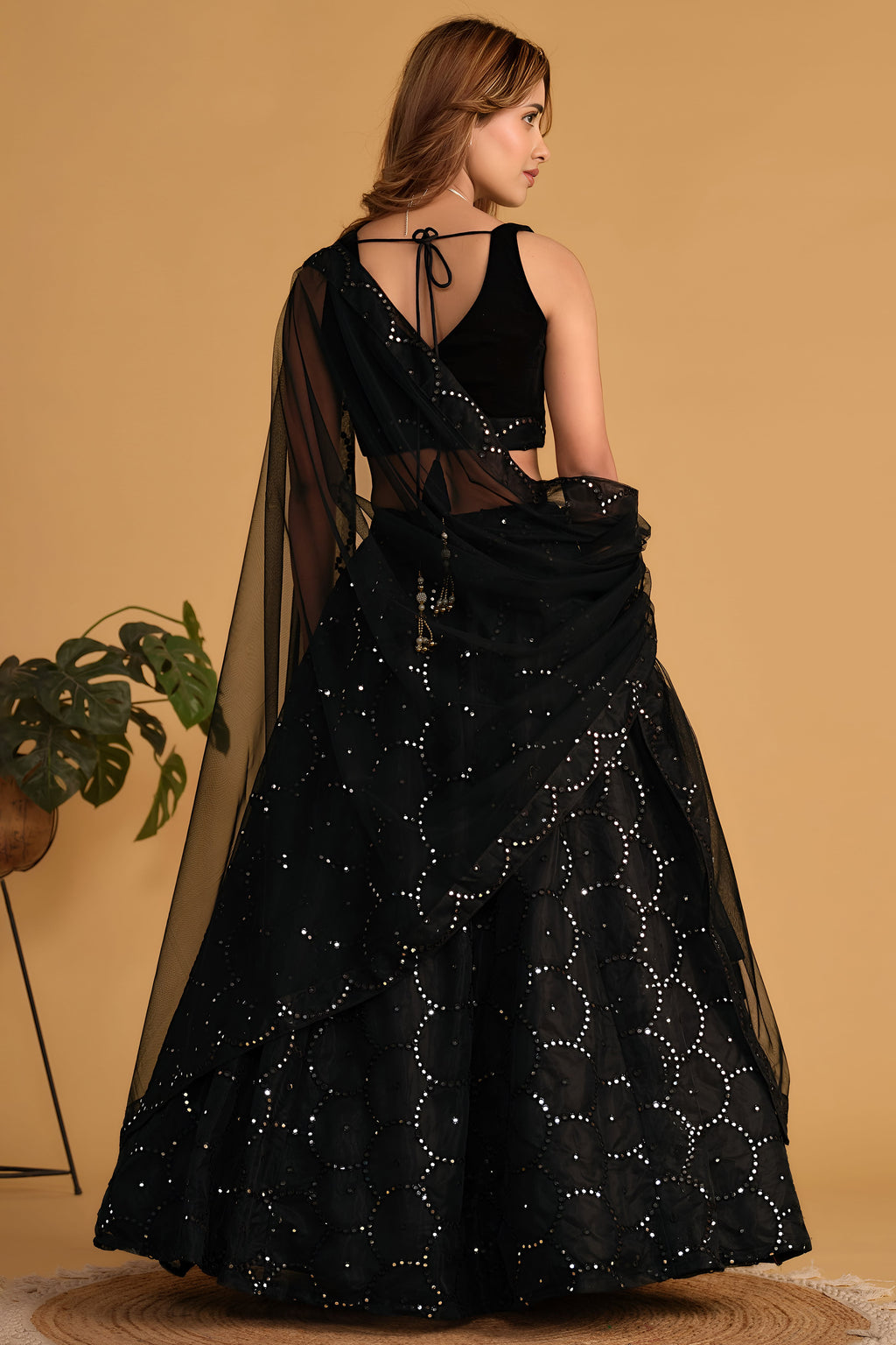 Full-length side view of a black cocktail lehenga with zari and sequin embroidery throughout on the flared organza lehenga skirt.