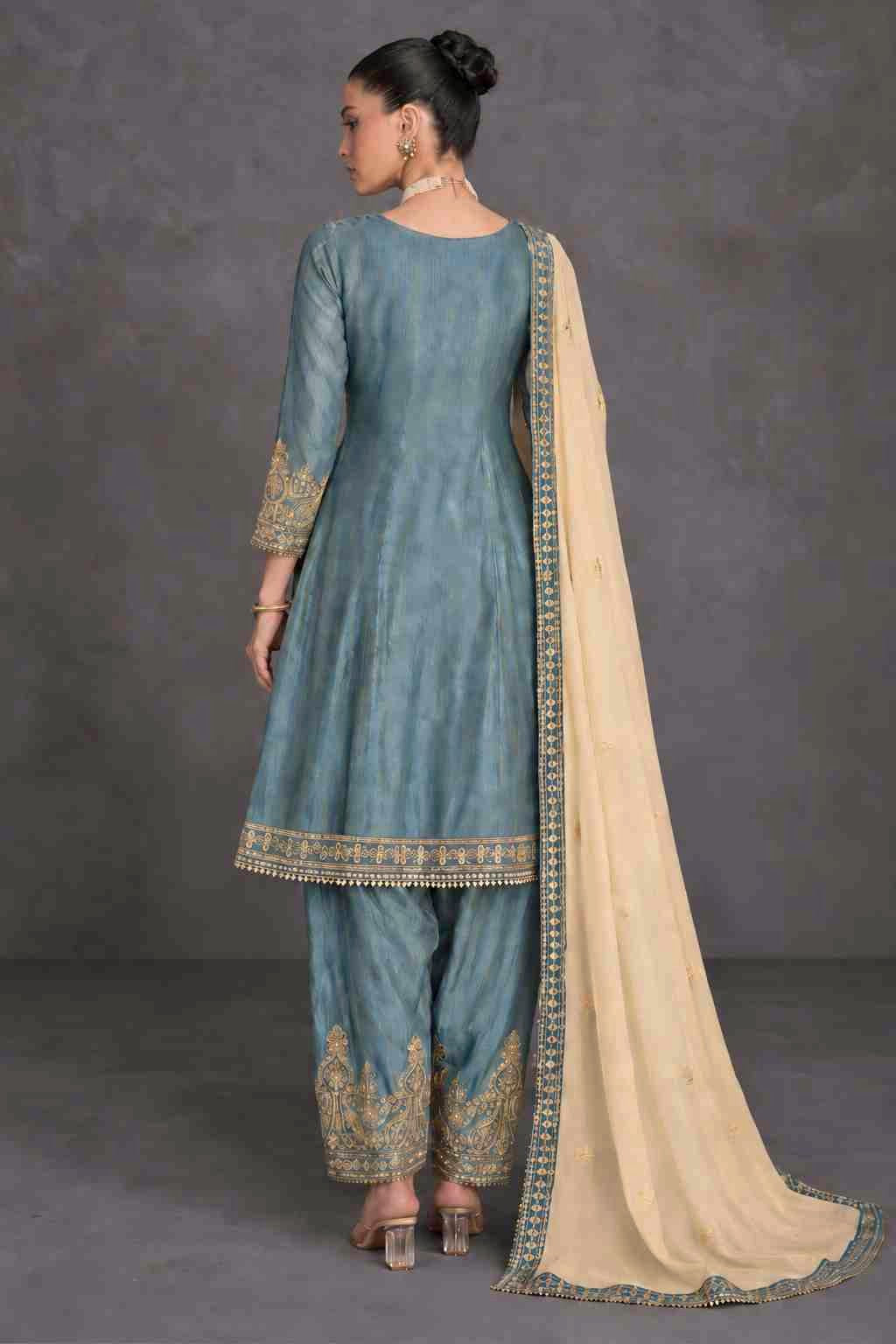 A woman modeling a traditional grey salwar kameez suit with gold embroidery and a cream dupatta, shown from the back against a studio backdrop.