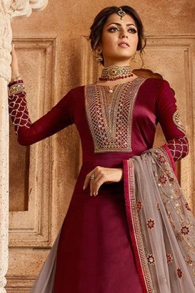 A woman poses in a closeup maroon kameez for women with ornate embroidery and a sheer dupatta against a carved architectural backdrop.