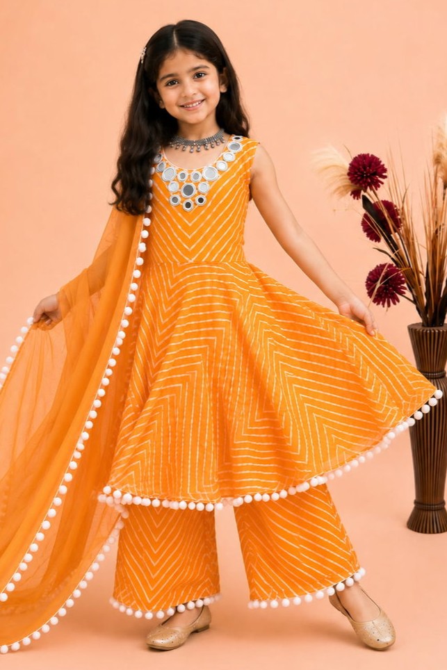 A kid modeling a orange traditional Indian outfit with white chevron patterns, white pom-pom trim, and a matching orange dupatta, set against a peach studio background.