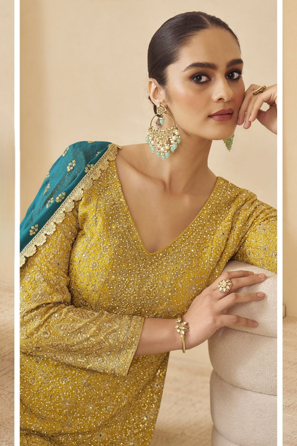 Woman wearing a yellow outfit for turmeric wedding ceremony against a beige background